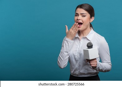 Waist Up Portrait Of Pretty Woman Reporter With Brown Hair, Who Interviews Someone Holding The Microphone And Is Yawning And Raising Her Right Hand To Her Mouth, Isolated On A Blue Background.