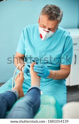 Waist up portrait of professional self confident male doctor in blue uniform and gloves doing pedicure in beauty clinic