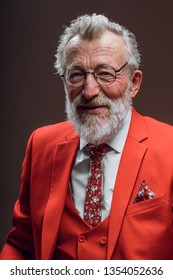 Waist Up Portrait Of Senior Chief Executive In Fashionable Red Suit With Necktie Smiling At Camera While Standing Against Yellow Background.