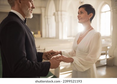 Waist up portrait of senior couple holding hands and exchanging wedding vows in church - Powered by Shutterstock