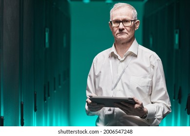 Waist Up Portrait Of Senior Data Scientist Looking At Camera And Holding Tablet While Working With Supercomputer In Futuristic Blue Light, Copy Space