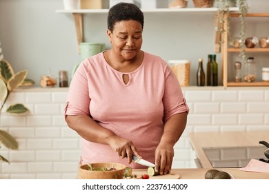 Waist up portrait of senior woman cutting vegetables while cooking in cozy home kitchen,copy space - Powered by Shutterstock