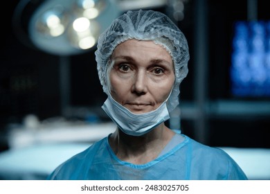 Waist up portrait of senior woman as female surgeon looking at camera standing in operating room and wearing mask, copy space - Powered by Shutterstock