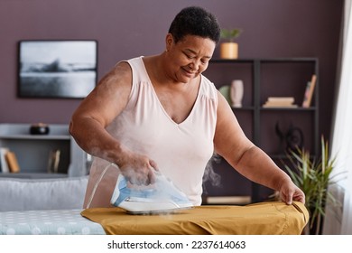 Waist up portrait of senior woman ironing clothes at home and smiling happily while caring for household - Powered by Shutterstock