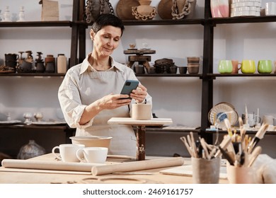 Waist up portrait of senior woman taking photos of handmade ceramics in art studio and posting on social media copy space - Powered by Shutterstock