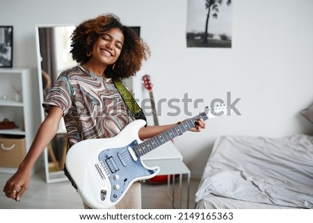 Waist up portrait of smiling African-American teenage girl playing electric guitar at home, copy space