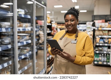 Waist up portrait of smiling black woman enjoying work in supermarket and looking at camera - Powered by Shutterstock