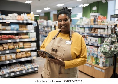 Waist up portrait of smiling black woman working in supermarket and looking at camera cheerfully - Powered by Shutterstock