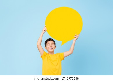 Waist up portrait of smiling cute Asian boy holding up an empty speech bubble in light blue studio background