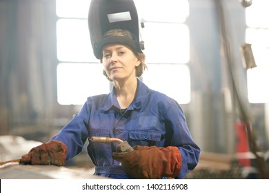 Waist up portrait of smiling female welder posing confidently while working at industrial plant or in garage, copy space