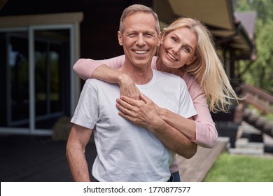 Waist up portrait of smiling loving couple standing and hugging while spending time outside holiday home