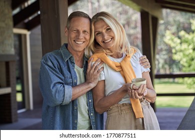 Waist up portrait of smiling man and woman embracing while drinking cup of coffee on terrace - Powered by Shutterstock