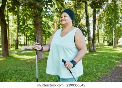 Waist Up Portrait Of Smiling Mature Black Woman Walking With Poles In Park During Outdoor Workout