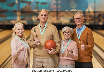 Waist Up Portrait Of Smiling Senior Team Wearing Medals Holding Trophy And Looking At Camera While Standing In Bowling Alley After Winning Match