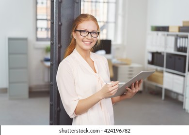 Waist Up Portrait of Smiling Young Businesswoman with Red Hair and Glasses Leaning Against Pole in Modern Office While Holding Handheld Tablet Computer - Shutterstock ID 424196782