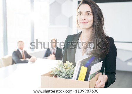 Waist up portrait of smiling young businesswoman holding box of personal belongings  leaving office after quitting job, copy space