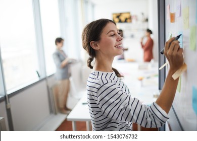Waist up portrait of smiling young woman writing on whiteboard in office, copy space