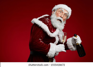 Waist Up Portrait Of Sneaky Santa Claus Holding Champagne Standing Against Red Background, Copy Space