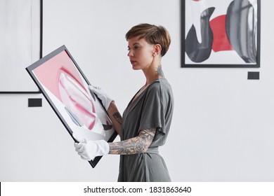 Waist up portrait of tattooed creative woman holding painting while planning art gallery exhibition, copy space
