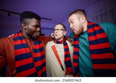 Waist up portrait of three excited sports fans huddling and cheering together at home wearing matching scarves in team colors - Powered by Shutterstock