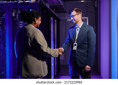 Waist up portrait of two business partners shaking hands while standing in data center interior - Powered by Shutterstock