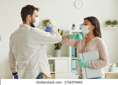 Waist up portrait of two colleagues wearing face masks bumping elbows while greeting each other at work in office - Powered by Shutterstock