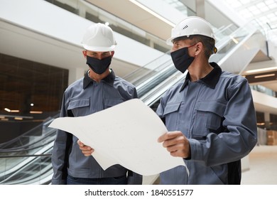 Waist Up Portrait Of Two Construction Workers Wearing Masks And Discussing Plans While Standing In Shopping Mall Or Office Building