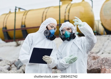Waist up portrait of two female scientists wearing hazmat suits collecting samples outdoors, toxic waste and pollution concept