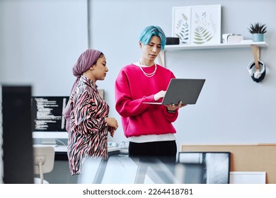 Waist up portrait of two gen Z young people using laptop white standing in office, focus on Asian man with colored hair - Powered by Shutterstock