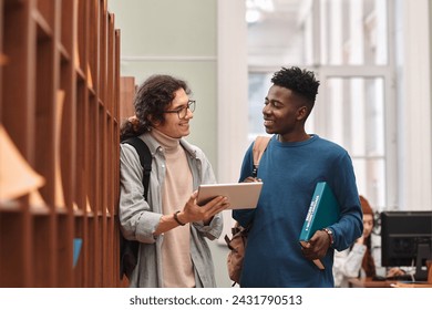 Waist up portrait of two smiling young men standing by shelves in college library and using digital tablet copy space - Powered by Shutterstock