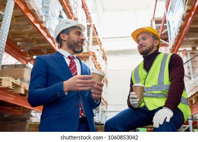 Waist Up Portrait Of Two Warehouse Workers Taking Break Sitting On Pellets Drinking Coffee And Chatting