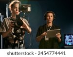 Waist up portrait of two women working in video production crew and operating camera on set