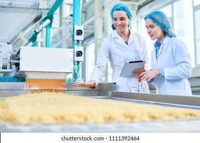 Waist up portrait of  two young female workers wearing lab coats standing by  conveyor line with macaroni  in clean production workshop, copy space - Powered by Shutterstock