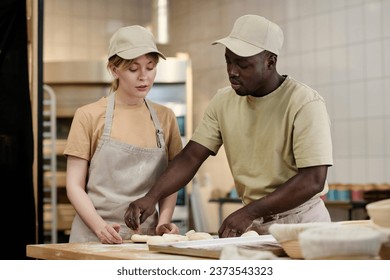 Waist up portrait of two young people working in bakery kitchen with young woman instructing trainee, copy space - Powered by Shutterstock