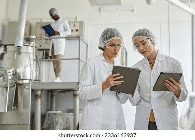 Waist up portrait of two young women wearing lab coats and using digital tablet in workshop of pharmaceutical factory, copy space - Powered by Shutterstock