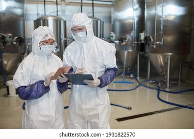 Waist up portrait of two young workers wearing hazmat suits while using digital tablet at chemical factory, copy space - Powered by Shutterstock