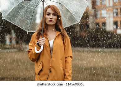 Waist up portrait of unhappy girl holding umbrella in hands. She is looking at camera with discontent 