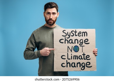 Waist Up Portrait View Of The Caucasian Worried Man Holding Carton Placard With System Change Not Climate Change Writing And Pointing At It With His Finger. 