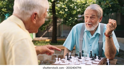 Waist up portrait view of the two caucasian old men neighbors sitting on a fresh air in their yard, talking and playing chess joyfully. Outdoors.  - Powered by Shutterstock