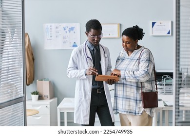 Waist up portrait of young African American doctor consulting female patient using digital tablet in clinic setting - Powered by Shutterstock