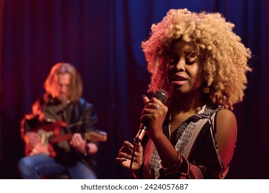 Waist up portrait of young African American woman with real hair texture singing into microphone on stage in nightclub copy space - Powered by Shutterstock