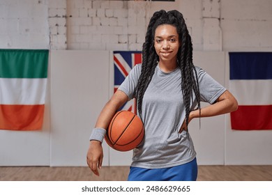 Waist up portrait of young African American woman as smiling basketball player holding ball and looking at camera posing in indoor court copy space - Powered by Shutterstock