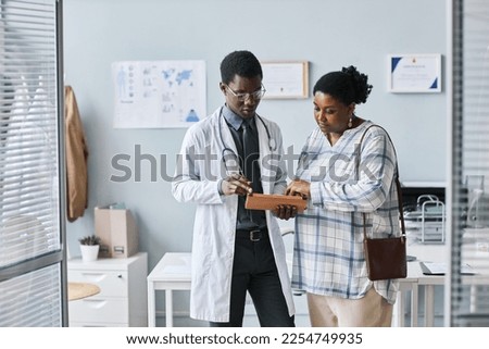 Waist up portrait of young African American doctor consulting female patient using digital tablet in clinic setting