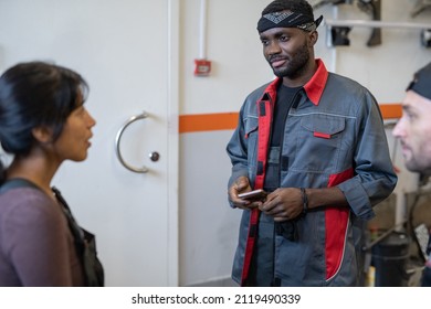 Waist up portrait of young African-American mechanic talking to colleagues while working in car repair shop