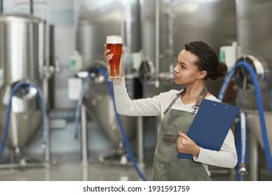 Waist up portrait of young African-American woman holding beer glass while inspecting quality of production at brewing factory, copy space - Powered by Shutterstock