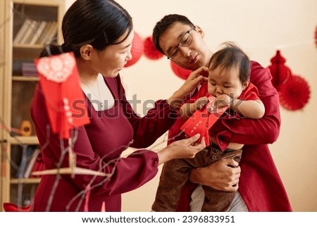 Waist up portrait of young Asian family with baby boy celebrating Chinese New Year together and holding traditional hongbao envelopes Translation Have overflowing abundance hundred years