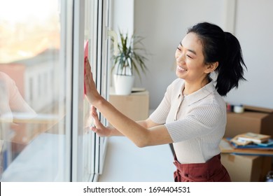 Waist Up Portrait Of Young Asian Woman Washing Windows While Enjoying Spring Cleaning In House Or Apartment, Copy Space