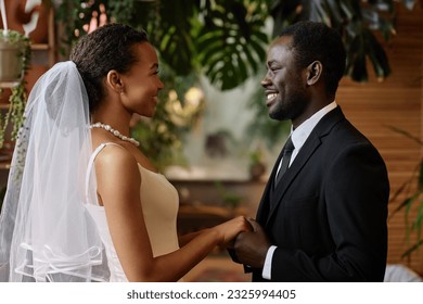 Waist up portrait of young black couple getting married and looking at each other holding hands - Powered by Shutterstock