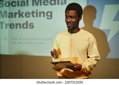 Waist Up Portrait Of Young Black Man Giving Presentation On Marketing While Standing By Projector Screen And Addressing Audience, Copy Space