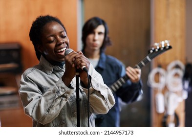 Waist Up Portrait Of Young Black Woman Singing To Microphone While Rehearsing With Band In Professional Recording Studio